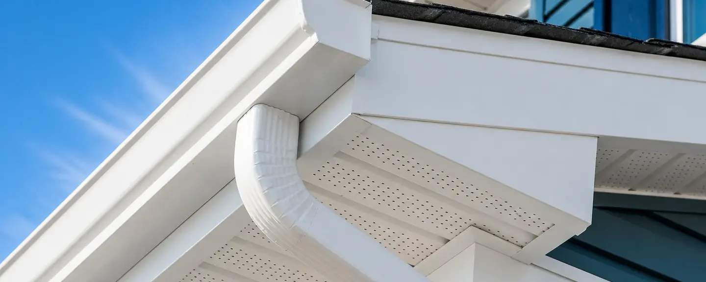 Dramatic upward view of a new white seamless gutter and downspout elbow at a roof corner.