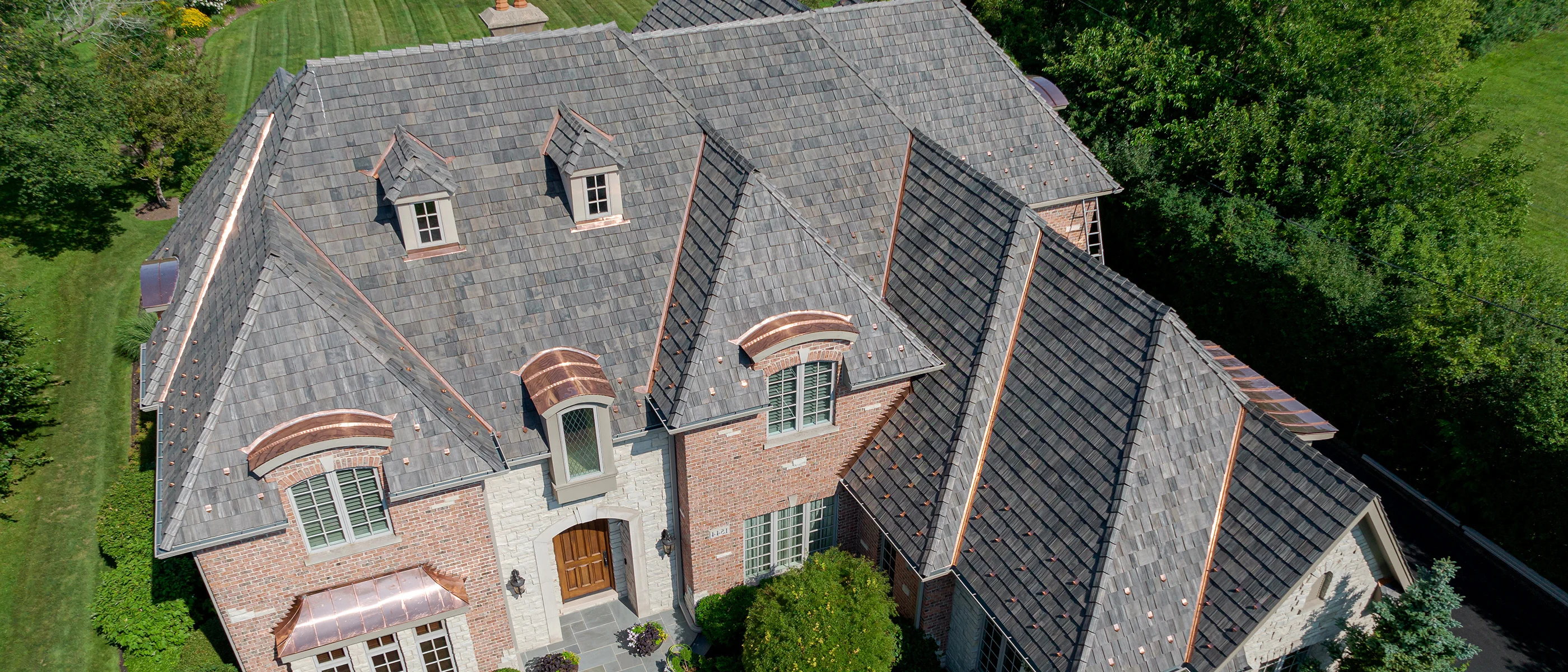 Aerial view of a brick and stone estate with a dark shake roof and copper accents.