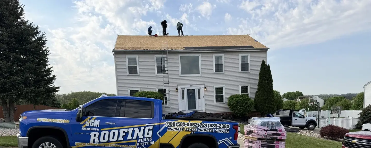 SGM Home Restoration crew tearing off a roof down to the decking with a branded company truck parked in the driveway.