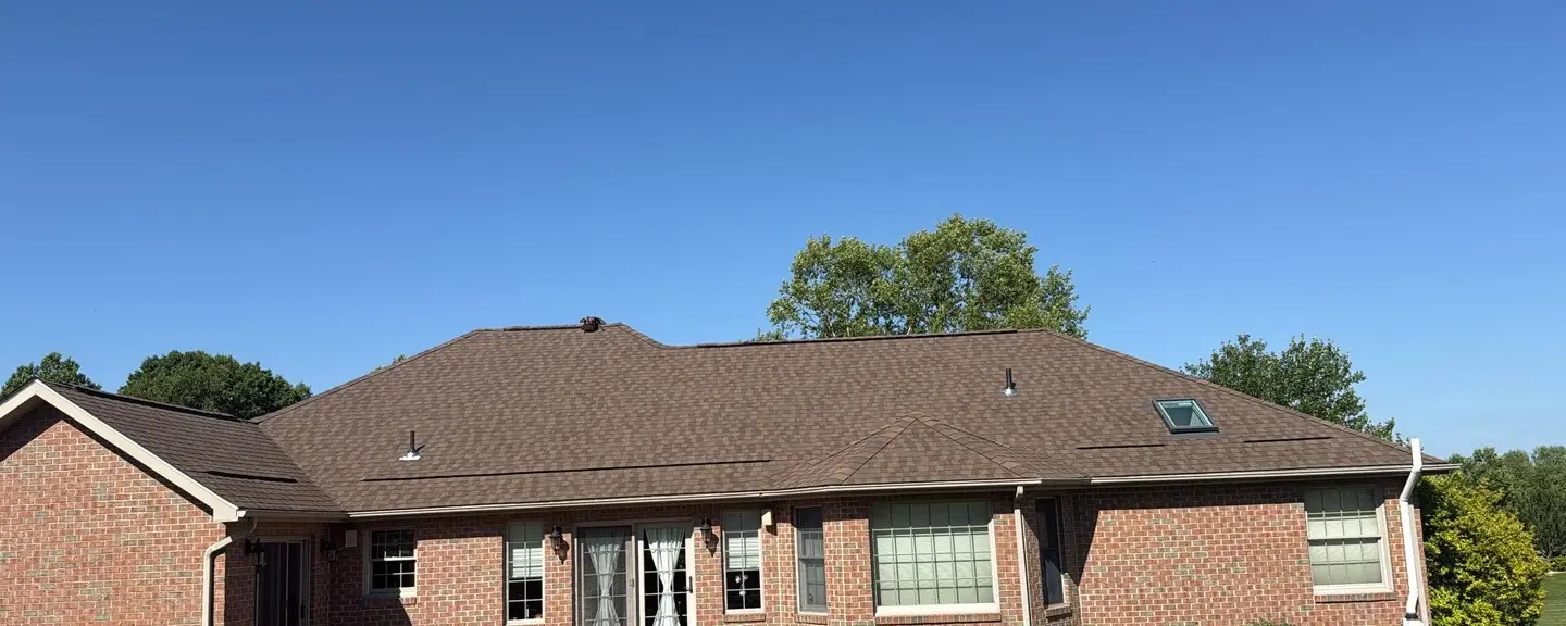 Brick ranch home with a complex hip roof and skylight under a clear blue sky.
