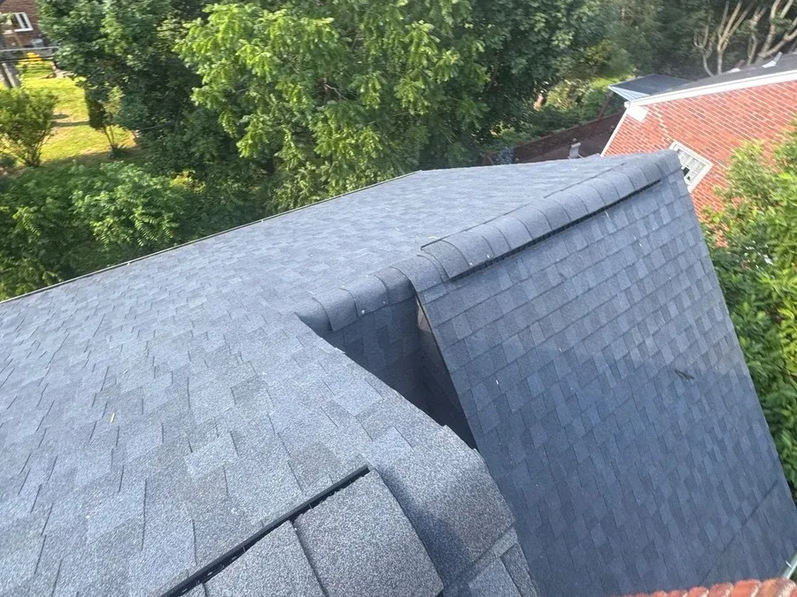 Finished valley and hip intersection on a shingle roof meeting cleanly beside a brick chimney.