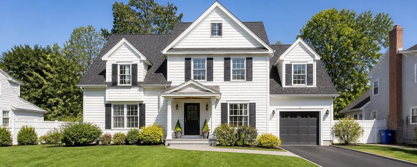 White cape cod style American home with a dark asphalt shingle roof and black shutters.