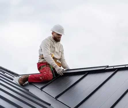 Roofer in a hard hat sitting on a standing-seam metal roof.