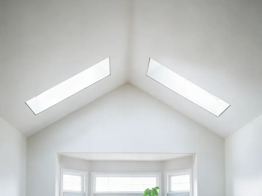 Interior view of a vaulted ceiling with two long skylights meeting at the ridge, bright natural light.