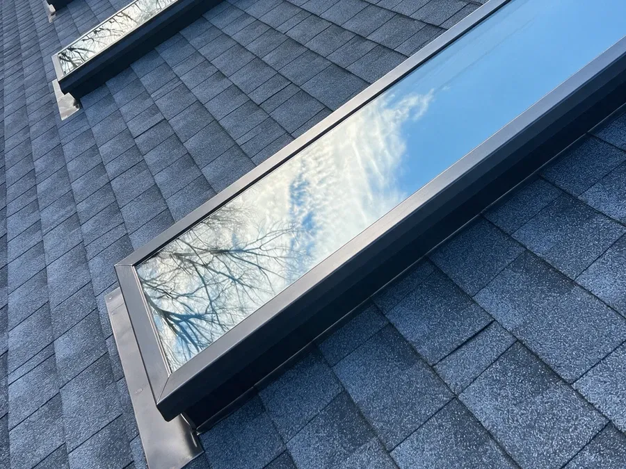 Close-up of a finished skylight window frame set into a dark gray asphalt shingle roof.