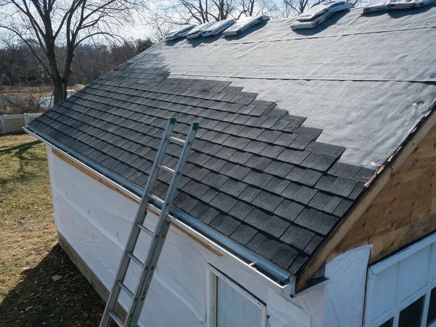 Roof replacement in progress, with new charcoal shingles installed on the lower half of the slope over gray underlayment and bundles staged near the ridge.