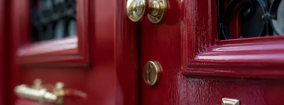 Close-up texture of a burgundy red front door with brass hardware.